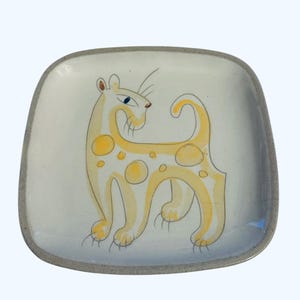 May include: Square ceramic plate with a hand-drawn illustration of a yellow cat with spots. The cat has blue eyes and a long tail. The plate has a gray border and a white background.