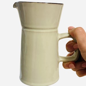 May include: A white ceramic pitcher with a brown rim and a handle. The pitcher has a slightly flared top and a cylindrical body.