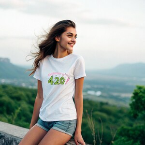 Pu&ograve; includere: T-shirt bianco con la scritta "Everyday is 4:20" in verde e rosa. La maglietta &egrave; a maniche corte e indossata con pantaloncini di jeans. Lo sfondo presenta un paesaggio sfocato con colline verdi e un cielo nuvoloso.