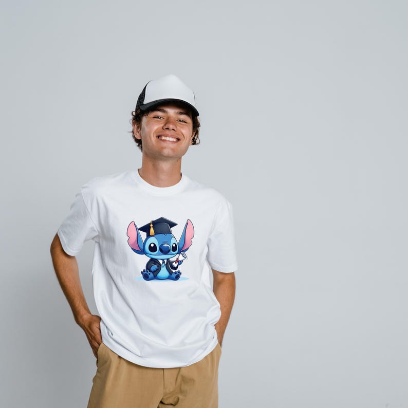 May include: White t-shirt featuring a cartoon character, Stitch, wearing a graduation cap and holding a diploma. The character is blue with pink ears and is wearing a graduation gown. The t-shirt is a classic crew neck style.