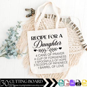 May include: A white tote bag with black text that reads "Recipe for a Daughter" and a list of ingredients for making a daughter, including "4 cans of prayer", "a cup of forgiveness", "2 spoonfuls of hope", "3 scoops of patience", and "1 barrel of love".