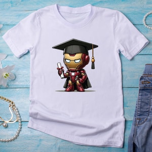 May include: White t-shirt featuring a cartoon Iron Man character wearing a graduation cap and holding a diploma. The Iron Man figure is in red, gold, and black. The shirt is made of a soft, lightweight material.