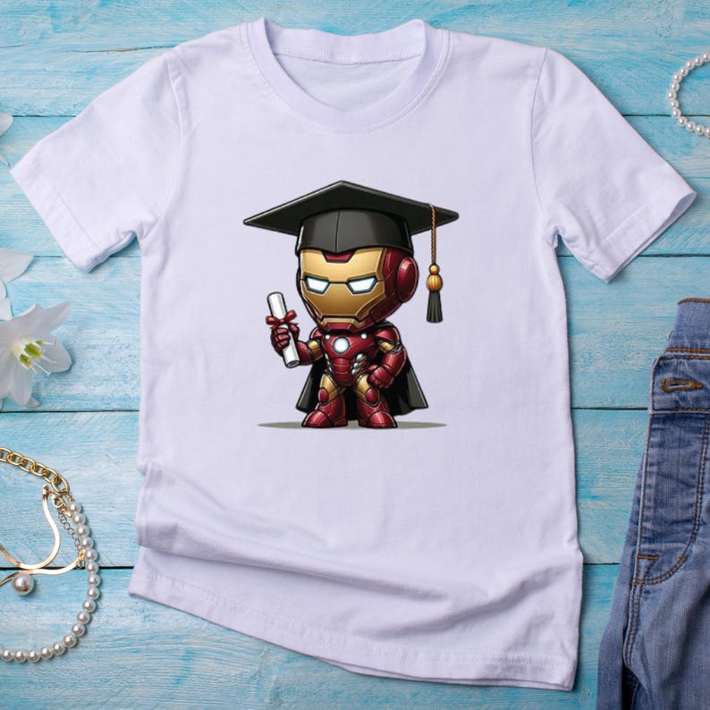 May include: White t-shirt featuring a cartoon Iron Man character wearing a graduation cap and holding a diploma. The Iron Man figure is in red, gold, and black. The shirt is made of a soft, lightweight material.