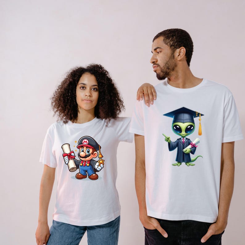 May include: Two white t-shirts with cartoon graphics. One shirt features Mario in a graduation cap holding a diploma and a star. The other shirt has an alien graduate in a cap and gown, holding a diploma.