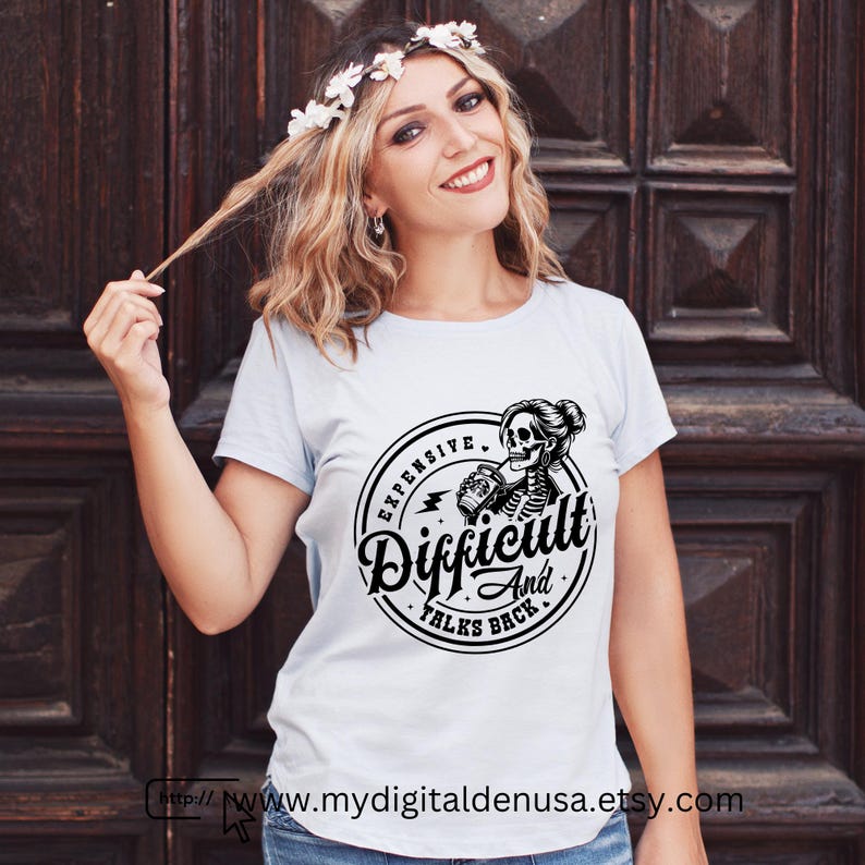 May include: A light blue t-shirt with a black and white graphic. The graphic is a circular design with the words "Expensive, Difficult, And Talks Back" surrounding a skeleton woman holding a can. The Etsy shop URL is visible.