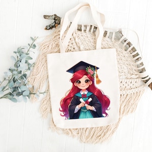 May include: Cream-colored tote bag featuring a cartoon illustration of a graduate with long red hair, wearing a graduation cap and gown, holding a diploma. The bag has cream-colored handles and is made of a sturdy fabric.