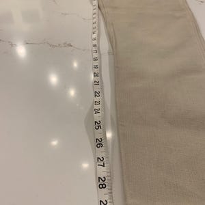 May include: Beige denim jeans with a straight leg, measured with a tape measure. The jeans are approximately 30 inches long. The fabric has a subtle texture, and the color is a light, neutral tone.