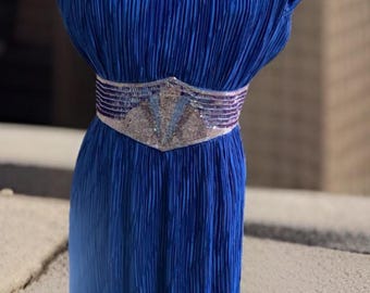 May include: A royal blue pleated dress with silver sequin accents on the shoulders and waist. The dress is displayed on a mannequin. The dress has a fitted waist and a flowing skirt. The dress is a vintage style.