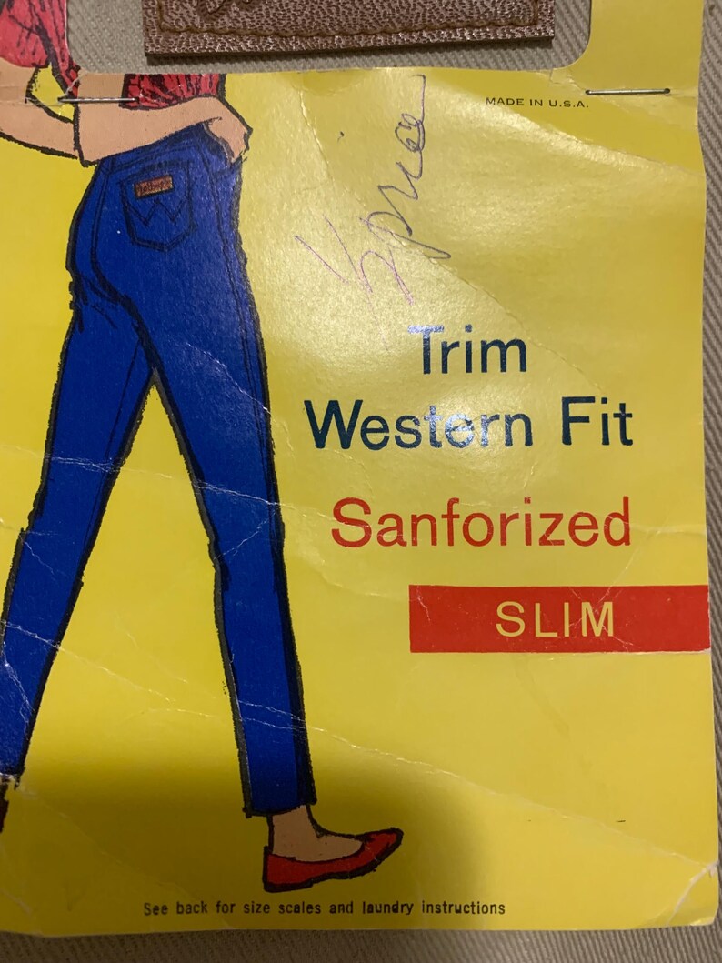 May include: A yellow paper with an illustration of blue jeans and the words "Trim Western Fit Sanforized SLIM." The text "MADE IN U.S.A." is at the top. A handwritten signature is visible.