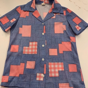 Puede incluir: Una camisa azul de manga corta con botones y un diseño de patchwork con cuadrados de cuadros rosa y blanco.