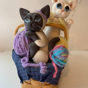 Gliniane koty w muzycznym koszyku wypełnionym włóczką, który gra „Favorite Things” autorstwa Cecila, podpisane przez artystę.