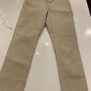 May include: Khaki-colored pants with a classic, straight-leg design. The pants feature a button and zipper closure, belt loops, and front and back pockets. The fabric appears to be a durable cotton or blend.