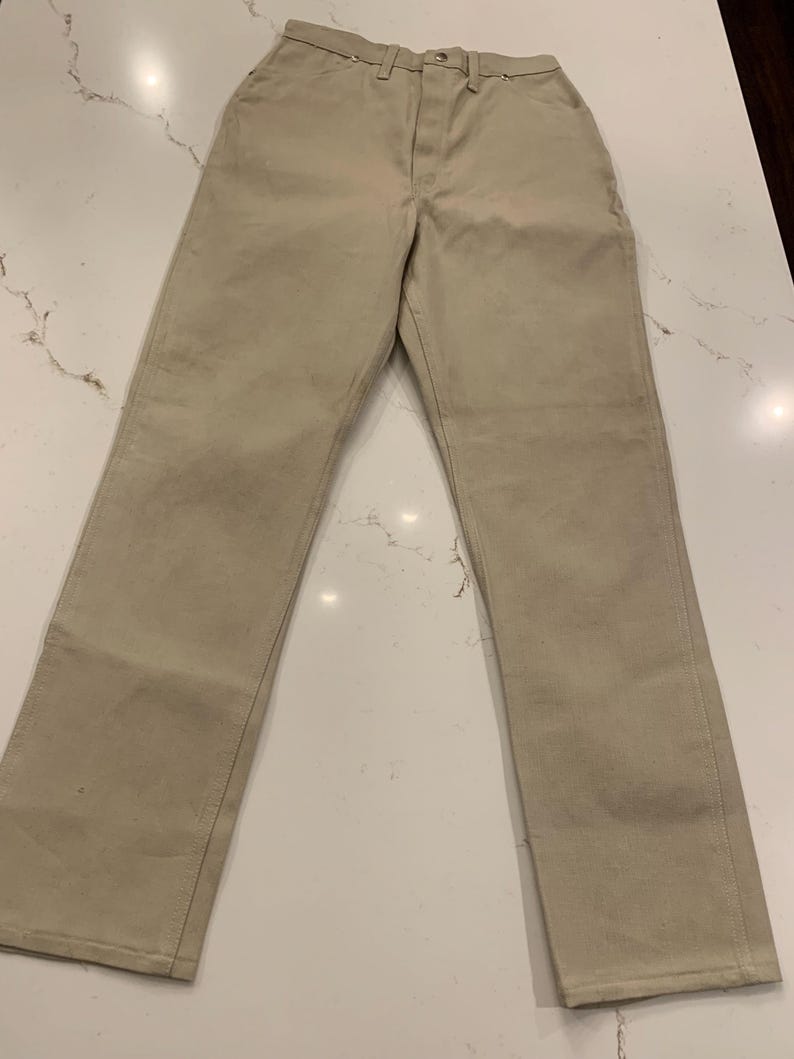 May include: Khaki-colored pants with a classic, straight-leg design. The pants feature a button and zipper closure, belt loops, and front and back pockets. The fabric appears to be a durable cotton or blend.
