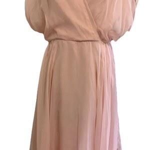 May include: A light pink vintage dress with a wrap-style bodice and a flowing skirt. The dress features short, puffy sleeves and a cinched waist. The fabric appears to be a lightweight, sheer material, creating a soft, elegant look. The dress is displayed on a mannequin.