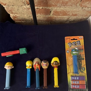Peut inclure: Une collection de distributeurs de bonbons Pez vintage représentant des personnages tels que Tweety Bird, Yosemite Sam, Taz et une Tortue Ninja. Les distributeurs sont dans leur emballage d'origine et sont en bon état.