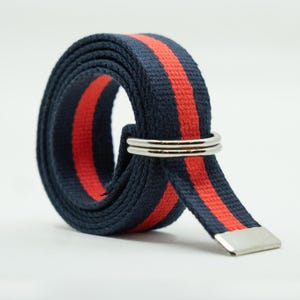 May include: A navy blue and red striped belt with a silver buckle. The belt is made of a woven fabric and has a simple design.