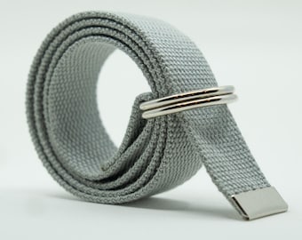 May include: A light gray woven fabric belt coiled into a circular shape. The belt features two polished silver-toned metal D-rings for closure and a matching silver-toned metal tip at the end of the strap to prevent fraying of the fabric material.
