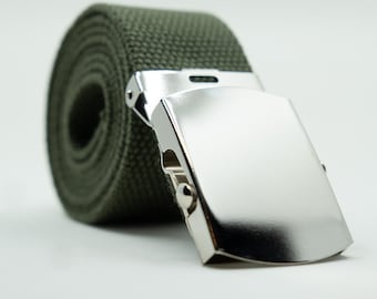 May include: A rolled-up olive green canvas belt with a shiny silver-colored buckle. The buckle is rectangular and has a smooth, reflective surface. The belt is made of a woven fabric.
