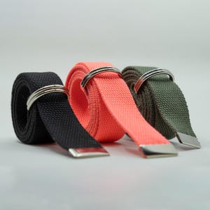 May include: Three fabric belts with silver metal buckles. The belts are black, coral, and olive green.
