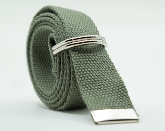 May include: A rolled-up olive green canvas belt with a silver-colored buckle and two silver loops. The belt is made of a woven fabric and has a rectangular metal end.