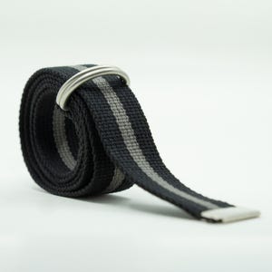 May include: A coiled belt made of black woven fabric featuring a central vertical gray stripe. The belt includes two silver-toned metal D-ring buckles at the top and a flat silver-toned metal tip at the end of the strap, creating a functional design.