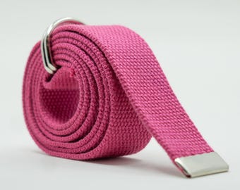 May include: A rolled-up, magenta-colored canvas belt with a silver-colored metal buckle and tip. The belt is made of a woven fabric and is designed to be worn around the waist. The belt is a solid color and has a simple, classic design.