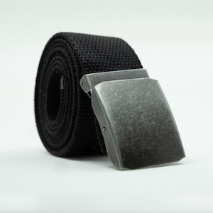 May include: A rolled-up black canvas belt with a silver-colored metal buckle. The belt is made of a woven fabric and has a rectangular buckle. The buckle is slightly open, suggesting it is ready to be fastened.
