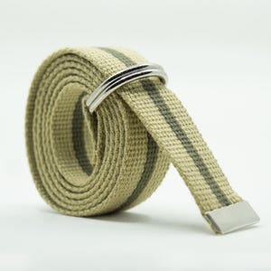 May include: A rolled-up canvas belt in a tan color with two dark green stripes. The belt features a silver-colored metal buckle and tip. The casual belt is suitable for everyday wear.