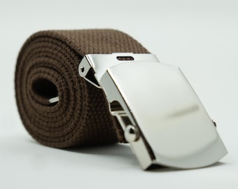 May include: A brown canvas belt rolled into a coil, featuring a polished silver-tone metal flip-top buckle. The belt strap has a visible woven texture and is secured by the metallic clasp, which is positioned in the foreground of the image.