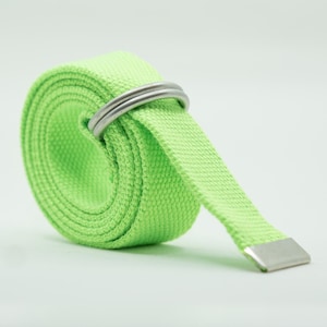 May include: A bright neon green woven fabric belt rolled into a circular shape. The belt features two silver-toned metal D-ring buckles at the top and a flat silver-toned metal tip at the end of the strap, providing a secure and adjustable closure.