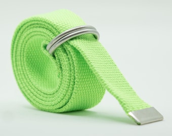 May include: A bright neon green woven fabric belt rolled into a circular shape. The belt features two silver-toned metal D-ring buckles at the top and a flat silver-toned metal tip at the end of the strap, providing a secure and adjustable closure.