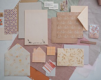May include: A collection of stationery items, including patterned paper, envelopes, and cards. The items feature floral, geometric, and bicycle patterns in shades of beige, peach, and white. Some pieces have illustrations of chickens and chicks.