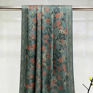 Puede incluir: Una tela color turquesa con un estampado floral de flores rosas y blancas y hojas verdes. La tela cuelga de una barra de metal. Los bordes de la tela tienen un borde decorativo.