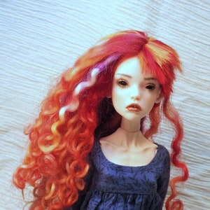 May include: A doll with long, curly red and yellow hair wearing a blue dress with a floral pattern.
