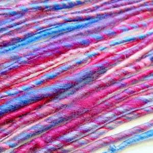 May include: A collection of colorful yarn strands in shades of pink, blue, and purple. The yarn is twisted and knotted, creating a textured and visually appealing look.