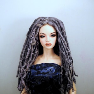 May include: A doll with long, gray dreadlocks and a strapless, dark blue velvet dress. The doll has detailed facial features, including blue eyes and full lips. The doll is a collectible item.