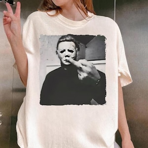 Op de afbeelding: Een wit T-shirt met een zwart-wit afbeelding van Michael Myers uit de Halloween-films die de middelvinger opsteekt.