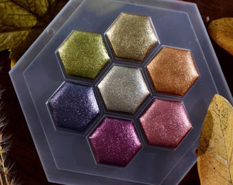 May include: A hexagonal palette with six metallic paint pans. The pans are arranged in a honeycomb pattern and are filled with shades of gold, silver, bronze, purple, and pink.