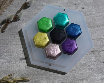 May include: A hexagonal tray with six hexagonal paint pans in various colors, including green, blue, purple, and gold. The tray is made of clear plastic and has a white background.