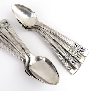 May include: A collection of silver spoons, some stacked and others fanned out. The spoons have a decorative floral design on the handle and a shiny, reflective surface. The spoons are arranged on a white background.