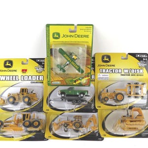 May include: A collection of John Deere die-cast metal toy vehicles, including a wheel loader, tractor with disk, and other construction equipment. The toys are in their original packaging, featuring the John Deere logo and product names.