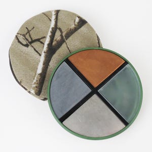 May include: A round, multi-colored sharpening stone set with a green rim and a camouflage-patterned cover. The stone is divided into four sections: copper, gray, and green. The cover is tan with a brown tree branch pattern.
