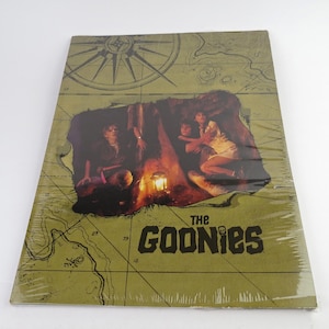 May include: A green and brown map with a compass and a torn section revealing a scene from the movie The Goonies. The title "The Goonies" is printed in black with a skull and crossbones.