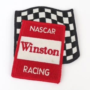 May include: Two embroidered patches. The first is a red rectangle with the words "NASCAR Winston RACING" in white. The second is a black and white checkered flag.