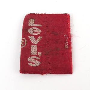 May include: A rectangular red fabric tag with the word "Levi's" in white lettering. The tag also features a small circular logo and the numbers "LT-503" printed vertically on the right side. The tag appears worn.