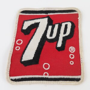 May include: A rectangular patch with a red background and the white and black "7 Up" logo. The patch has a white border and several white circles. The "R" registered trademark symbol is visible.