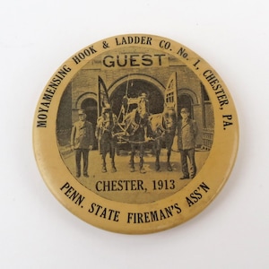 May include: A round, tan-colored pinback button featuring a black-and-white historical image of a horse-drawn fire carriage with two people standing beside it. The text reads MOYAMENSING HOOK & LADDER CO. No. 1, CHESTER, PA., GUEST, and CHESTER, 1913, PENN. STATE FIREMAN'S ASS'N.