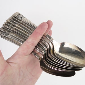 May include: A collection of silver spoons, held in a hand. The spoons have a decorative floral design on the handle and a shiny, reflective surface. The spoons are likely vintage or antique.