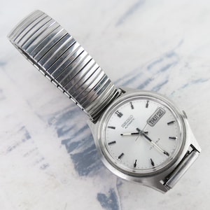 May include: A silver Seiko automatic wristwatch with a white face, black hands, and a date window displaying "THU 2". The watch has a silver metal band.