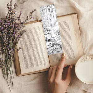 May include: A bookmark featuring a cozy reading scene with a cup of coffee, glasses, and a book. The bookmark is placed in an open book, next to a bouquet of lavender and a cup of coffee with milk.